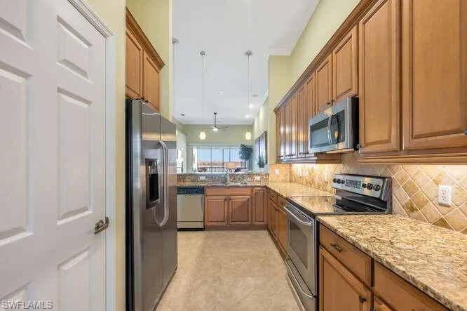 Kitchen featuring appliances with stainless steel finishes, brown cabinets, backsplash, light stone countertops, and a sink
