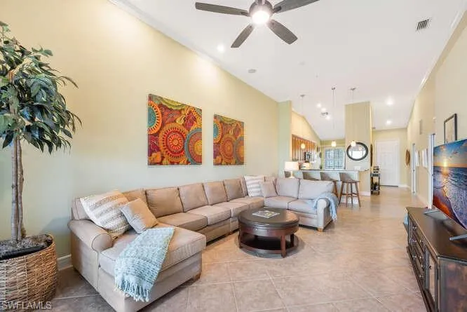 Living room with ceiling fan, light tile patterned flooring, visible vents, baseboards, and vaulted ceiling
