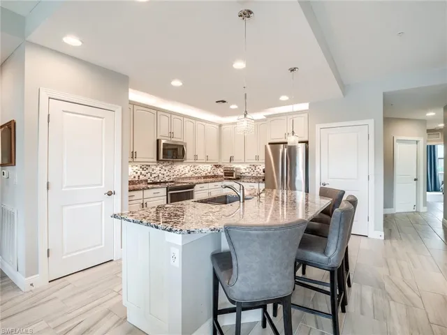 Kitchen featuring appliances with stainless steel finishes, a kitchen island with sink, a breakfast bar area, pendant lighting, and tasteful backsplash