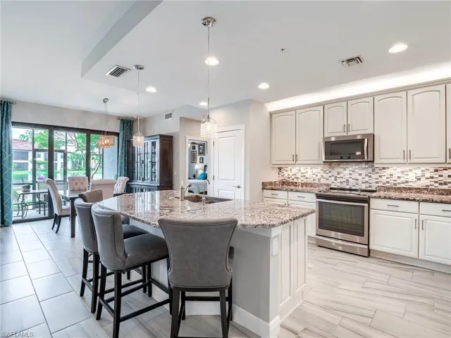 Kitchen with tasteful backsplash, hanging light fixtures, sink, a kitchen island with sink, and appliances with stainless steel finishes