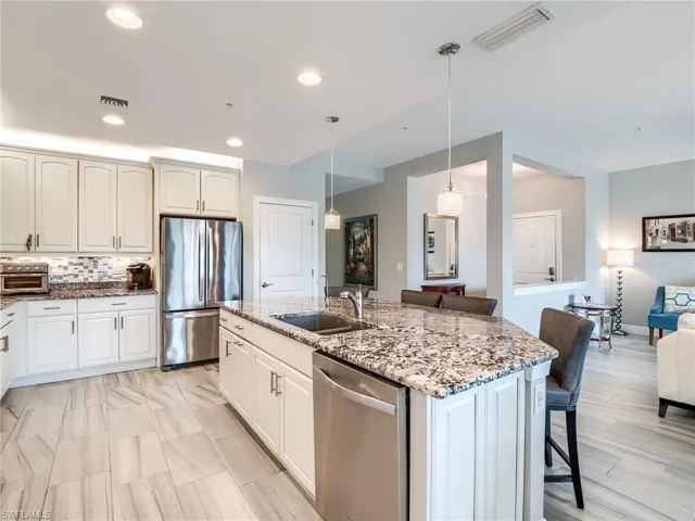 Kitchen with light stone countertops, an island with sink, pendant lighting, sink, and appliances with stainless steel finishes