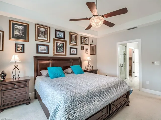Bedroom with light carpet, ensuite bathroom, and ceiling fan