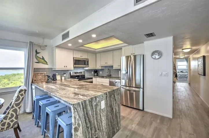 Kitchen featuring stainless steel appliances, light stone countertops, a peninsula, a kitchen bar, and a raised ceiling