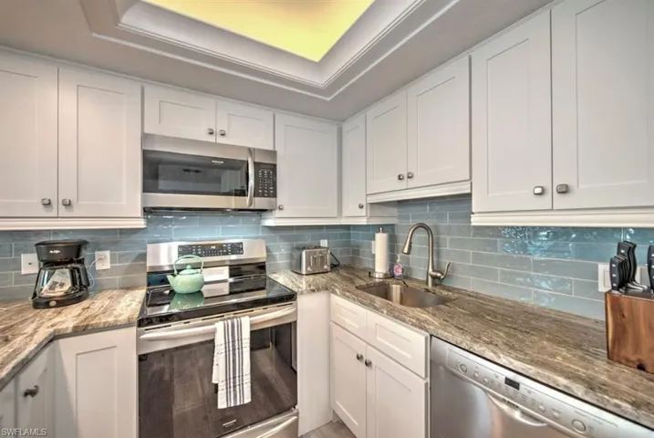 Kitchen featuring appliances with stainless steel finishes, white cabinets, light stone counters, and tasteful backsplash