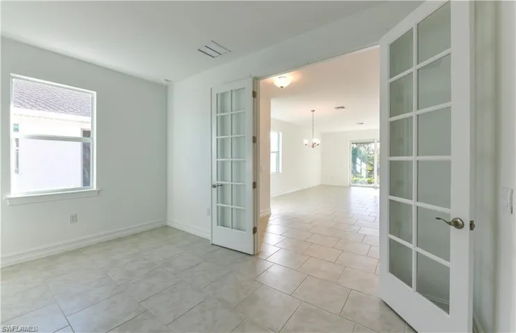 Spare room featuring light tile patterned floors, french doors, and a chandelier