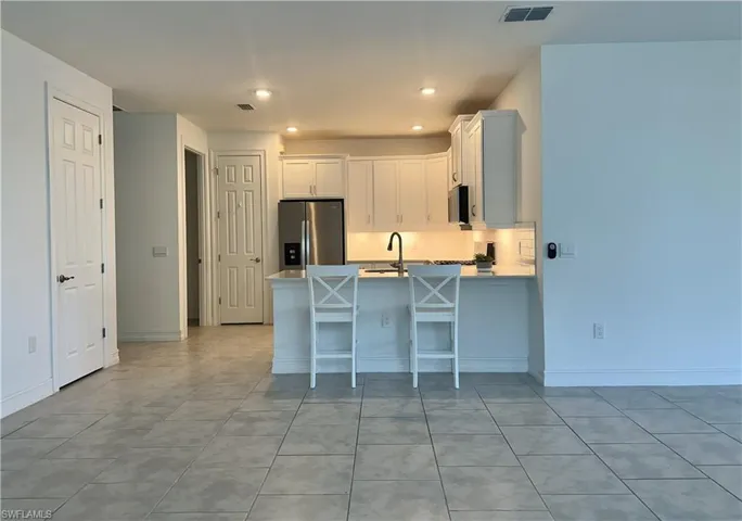 Kitchen with white cabinetry, stainless steel appliances, a peninsula, a kitchen bar, and light tile patterned flooring