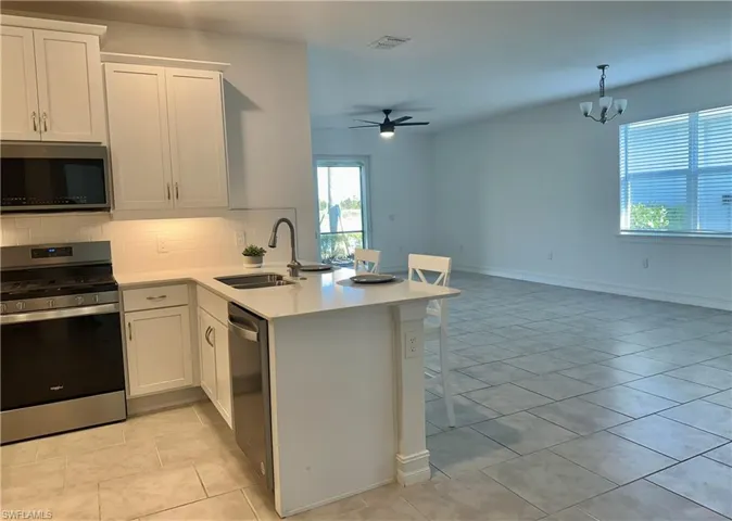 Kitchen with appliances with stainless steel finishes, white cabinetry, a kitchen breakfast bar, tasteful backsplash, and ceiling fan