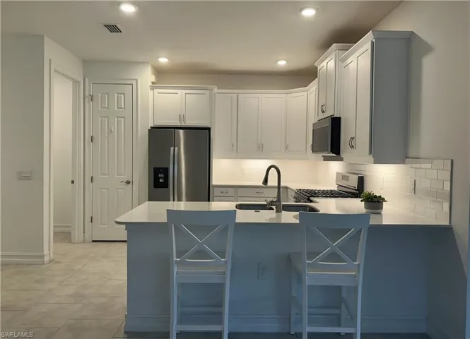 Kitchen featuring stainless steel appliances, a kitchen breakfast bar, white cabinets, a peninsula, and recessed lighting