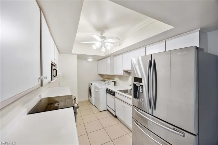Kitchen with stainless steel appliances, white cabinets, light countertops, a tray ceiling, and light tile patterned floors