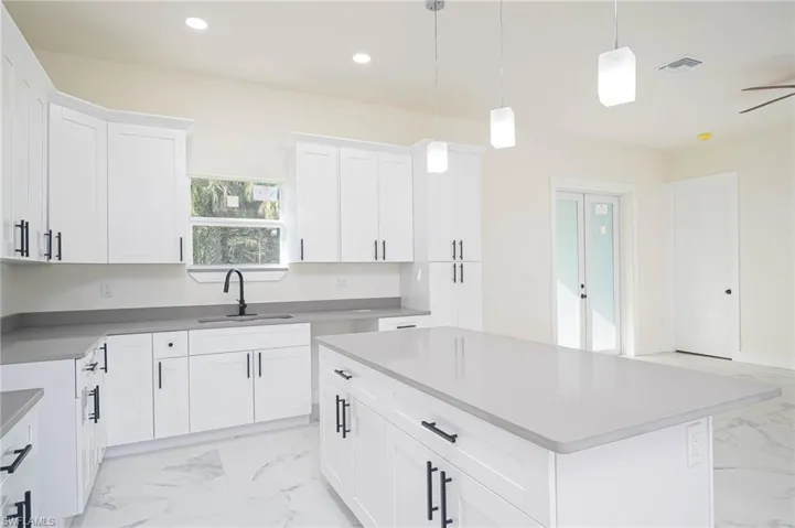 Kitchen featuring a center island, hanging light fixtures, sink, ceiling fan, and white cabinetry