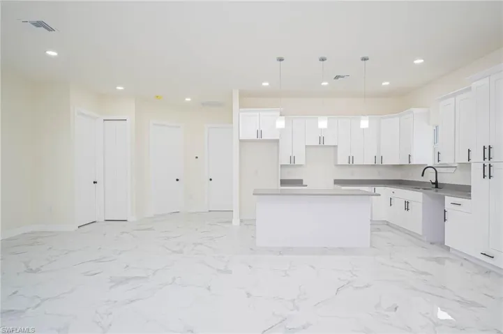Kitchen with white cabinets, hanging light fixtures, sink, and a center island