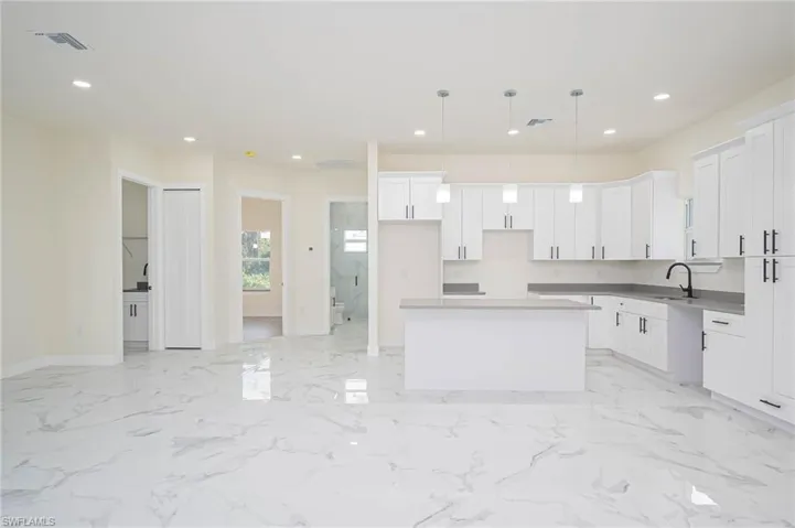 Kitchen featuring a kitchen island, hanging light fixtures, sink, and white cabinets