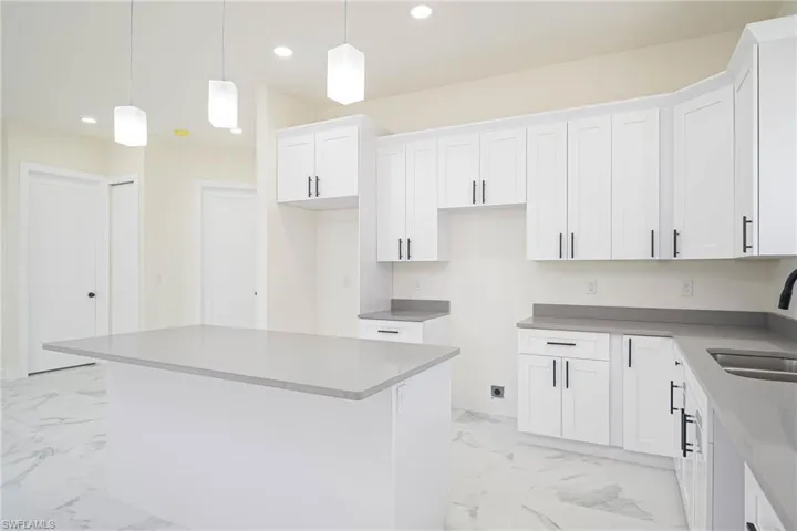 Kitchen with white cabinetry, sink, pendant lighting, and a kitchen island