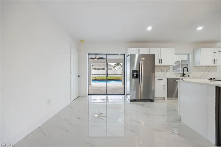 Kitchen featuring light marble finish floors, stainless steel appliances, white cabinetry, light stone counters, and recessed lighting
