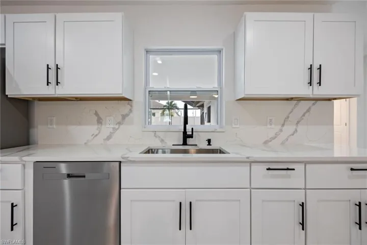 Kitchen featuring stainless steel dishwasher, white cabinets, light stone countertops, and decorative backsplash