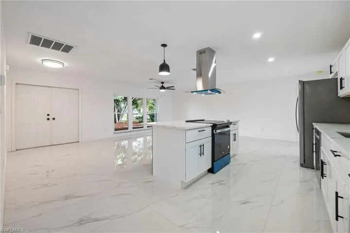 Kitchen with light marble finish floors, white cabinetry, appliances with stainless steel finishes, a center island with sink, and pendant lighting