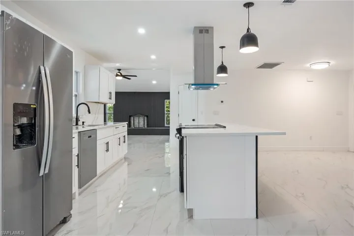 Kitchen with appliances with stainless steel finishes, white cabinetry, recessed lighting, pendant lighting, and light marble finish flooring