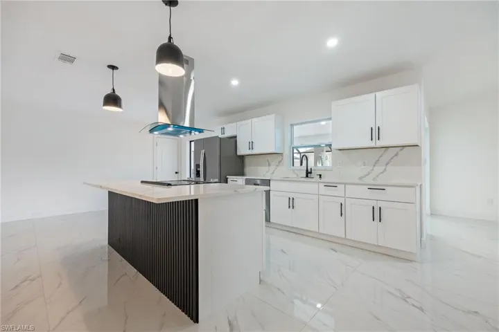 Kitchen featuring light marble finish flooring, white cabinetry, a center island, decorative light fixtures, and appliances with stainless steel finishes