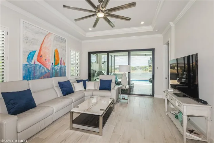 Living area featuring plenty of natural light, a ceiling fan, a tray ceiling, and ornamental molding