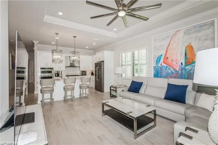 Living room featuring a raised ceiling, ceiling fan, a chandelier, ornamental molding, and recessed lighting