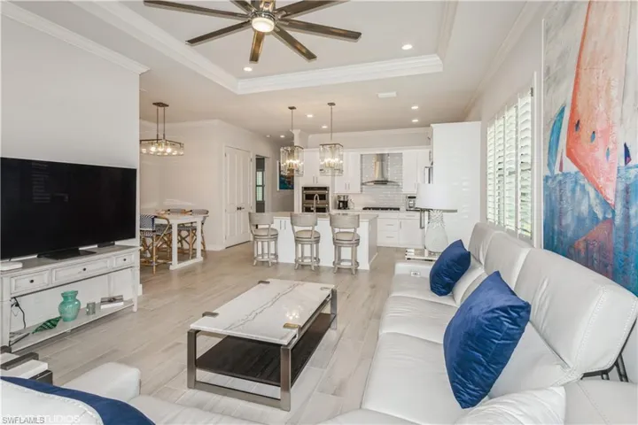 Living room featuring a raised ceiling, a ceiling fan, crown molding, a chandelier, and light wood-type flooring