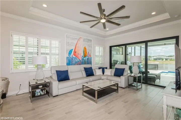 Living room featuring a raised ceiling, ceiling fan, light wood finished floors, and ornamental molding