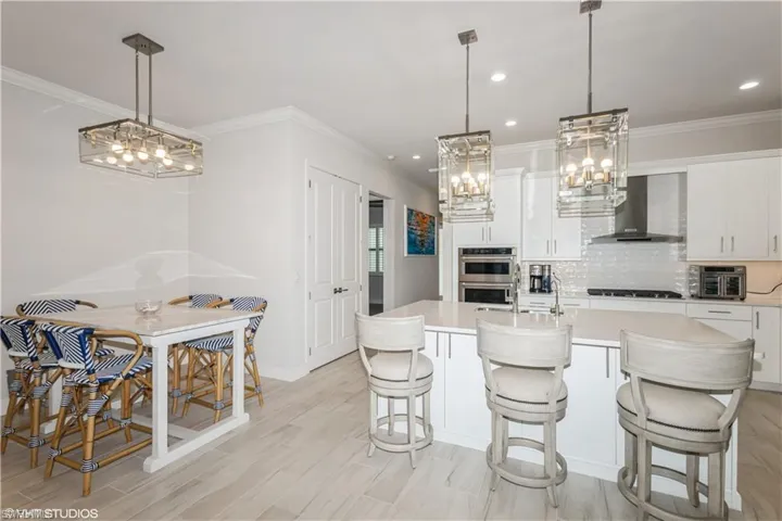 Kitchen featuring wall chimney range hood, light countertops, backsplash, ornamental molding, and white cabinetry