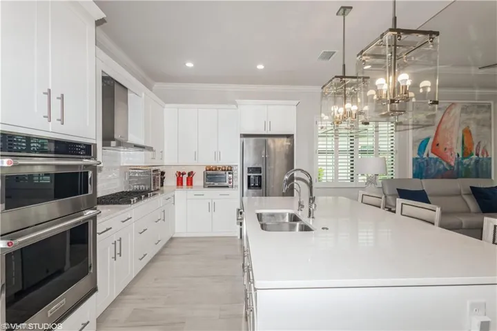 Kitchen featuring wall chimney exhaust hood, a sink, stainless steel appliances, ornamental molding, and a center island with sink