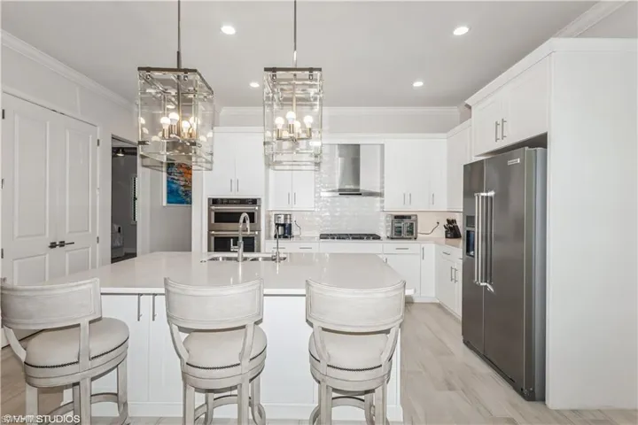 Kitchen featuring stainless steel appliances, wall chimney exhaust hood, a sink, light countertops, and tasteful backsplash