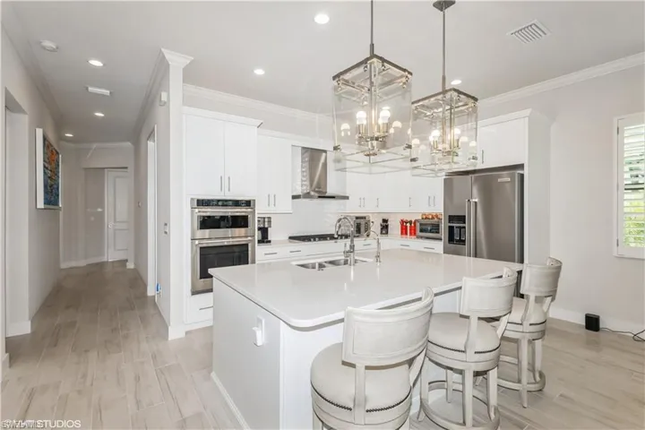 Kitchen with wall chimney exhaust hood, stainless steel appliances, a chandelier, an island with sink, and light countertops