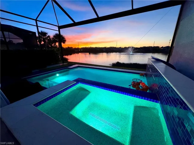 Pool at dusk with a water view, a pool with connected hot tub, a sunroom, and a lanai