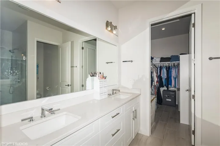 Full bath featuring a shower with shower door, toilet, double vanity, and a spacious closet