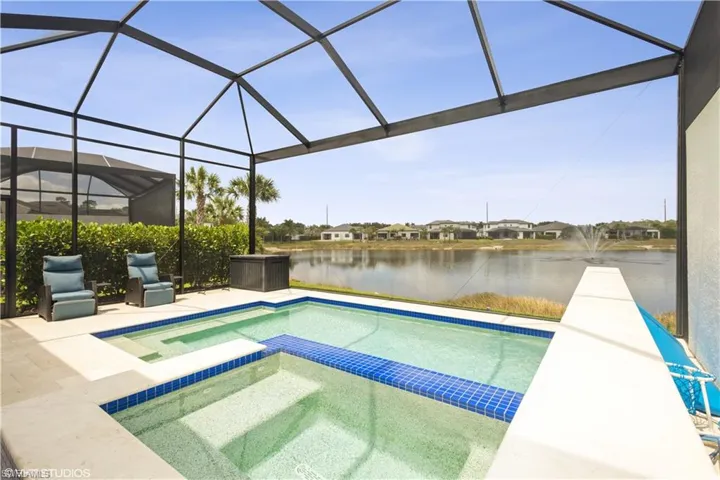 View of pool with a water view, a pool with connected hot tub, glass enclosure, and a patio area