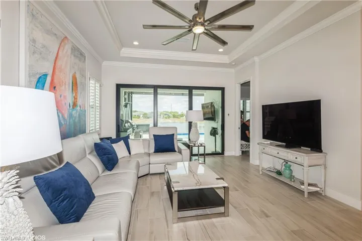 Living area with a ceiling fan, a tray ceiling, crown molding, baseboards, and light wood-style floors