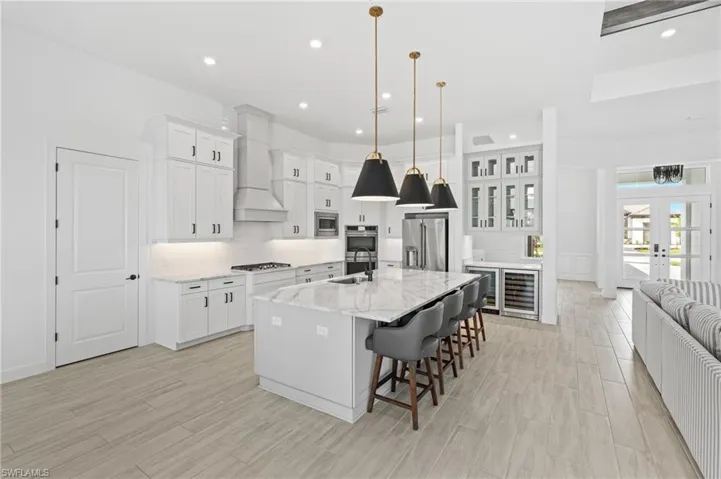 Kitchen featuring a breakfast bar, white cabinets, a center island with sink, wood finish floors, and wine cooler