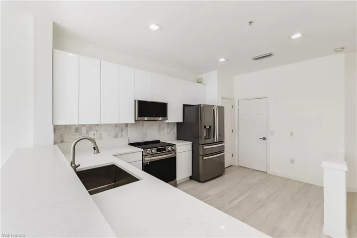 Kitchen with backsplash, appliances with stainless steel finishes, white cabinets, modern cabinets, a pantry and polished marble tile flooring.