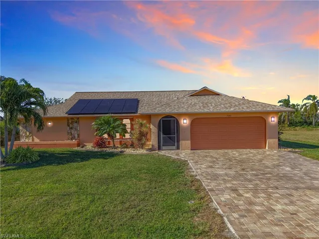 Single story home with a lawn, solar panels, and a garage