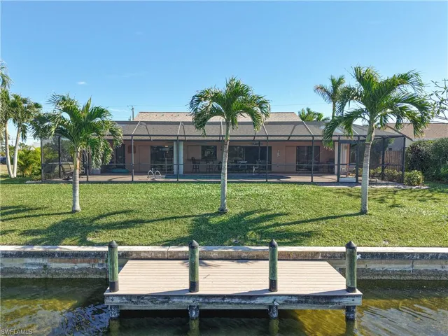 View of dock with a lawn, glass enclosure, and a water view