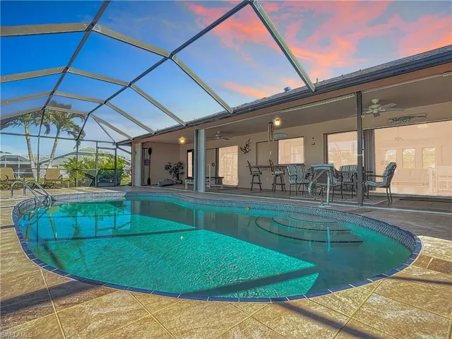 Pool at dusk with a lanai, a patio area, and ceiling fan