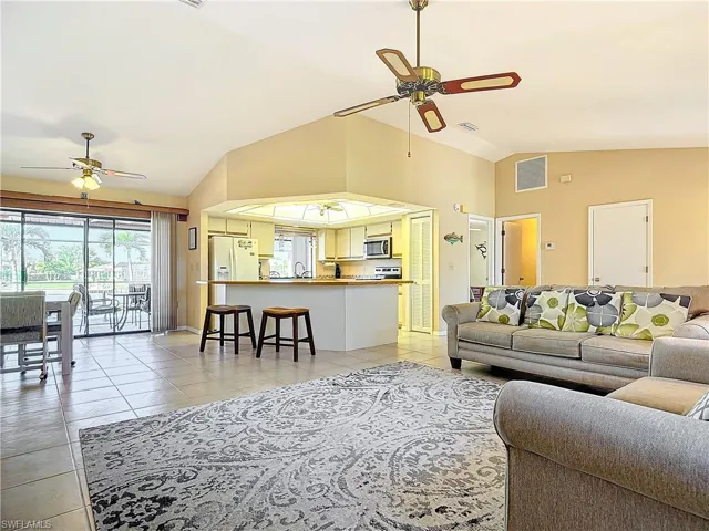 Living room featuring light tile patterned floors, ceiling fan, lofted ceiling, and sink