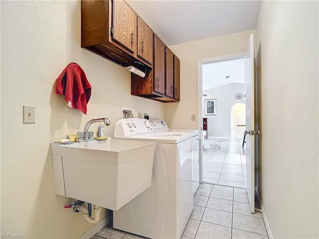 Clothes washing area with cabinets, sink, separate washer and dryer, and light tile patterned flooring
