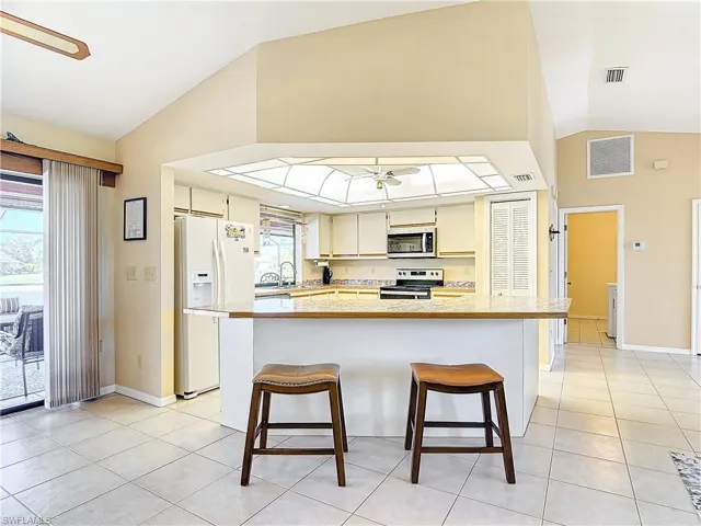 Kitchen with a kitchen bar, stainless steel appliances, ceiling fan, sink, and light tile patterned floors