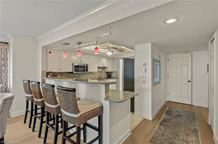 Kitchen with ceiling fan, decorative light fixtures, light hardwood / wood-style floors, a kitchen bar, and white cabinetry