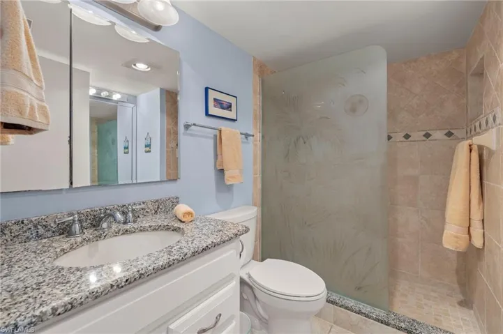 Bathroom with tiled shower, vanity, toilet, and tile patterned flooring
