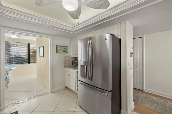 Kitchen with decorative backsplash, stainless steel refrigerator with ice dispenser, ceiling fan, light tile patterned floors, and white cabinets