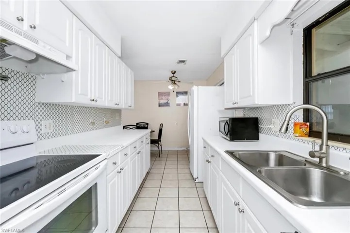 Kitchen with white electric range oven, a sink, light countertops, tasteful backsplash, and under cabinet range hood