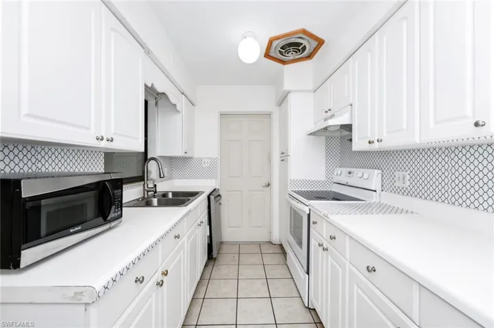 Kitchen with under cabinet range hood, stainless steel appliances, decorative backsplash, and a sink