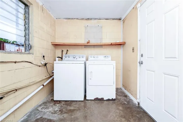 Laundry room with concrete block wall, laundry area, and washing machine and clothes dryer