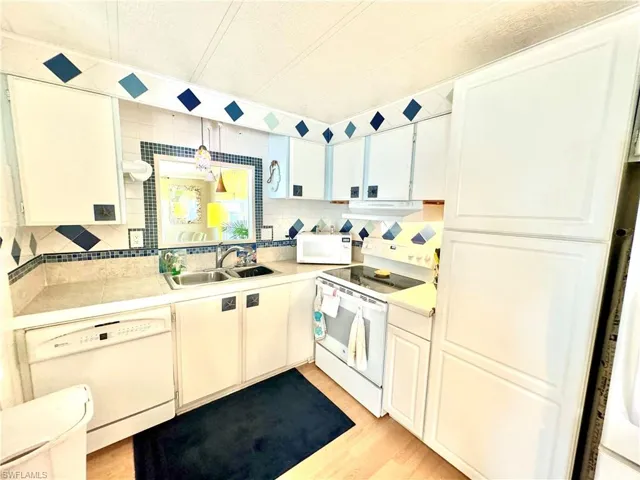 Kitchen featuring light hardwood / wood-style flooring, tasteful backsplash, white appliances, range hood, and sink
