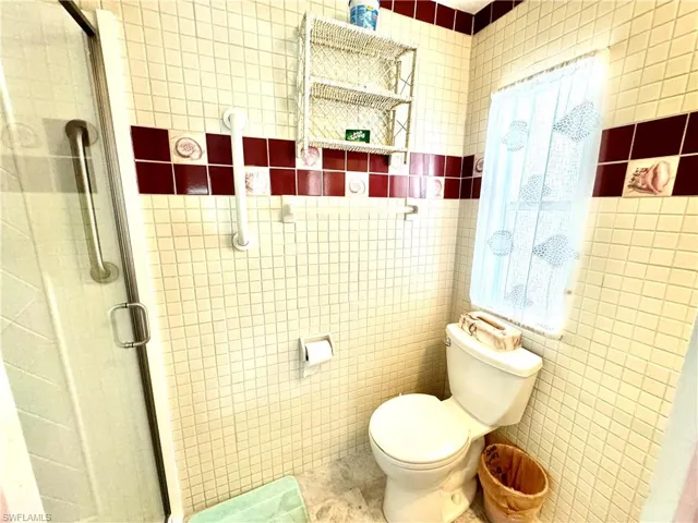 Master Bathroom featuring a shower with door, tile flooring, toilet, and tile walls